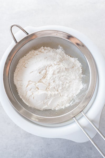 dry ingredients are being sifted into wet ingredients