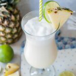 One glass with pina colada drink garnished with pineapple wedge and lime slice.