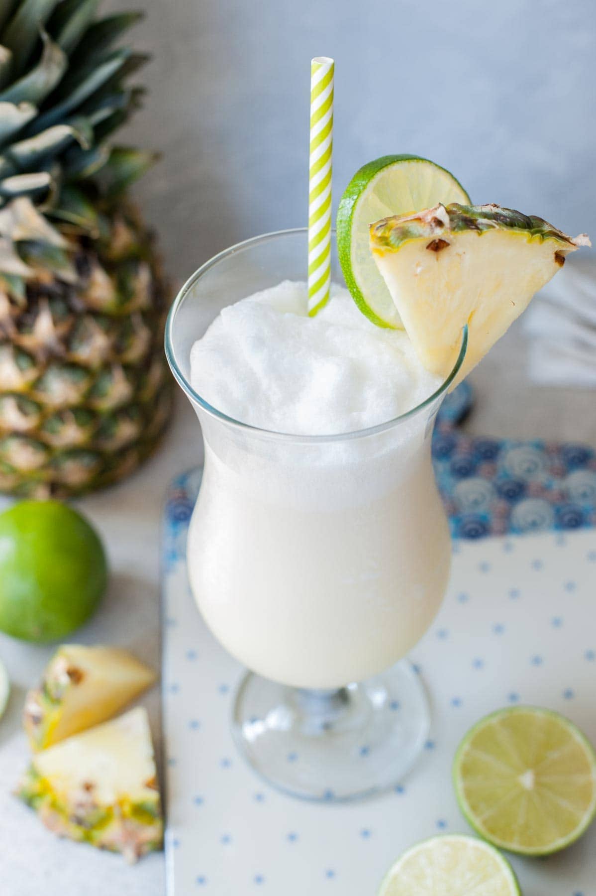 One glass with pina colada drink garnished with pineapple wedge and lime slice.