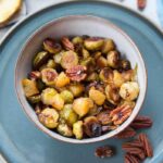 Roasted brussel sprouts with pineapple and pecans in a grey bowl.