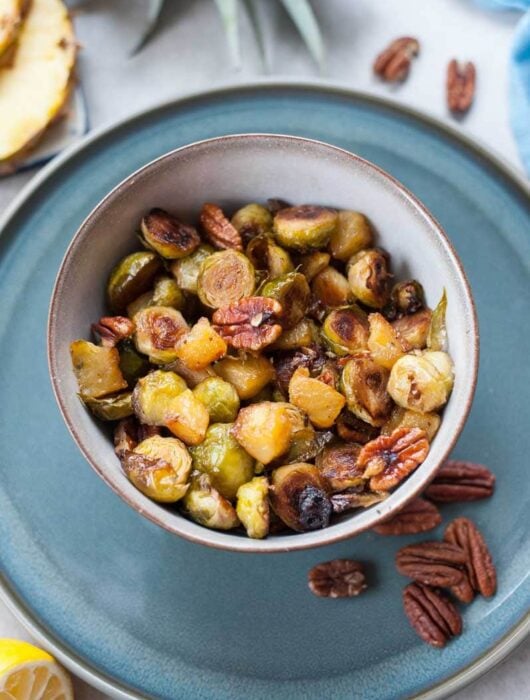Roasted brussel sprouts with pineapple and pecans in a grey bowl.