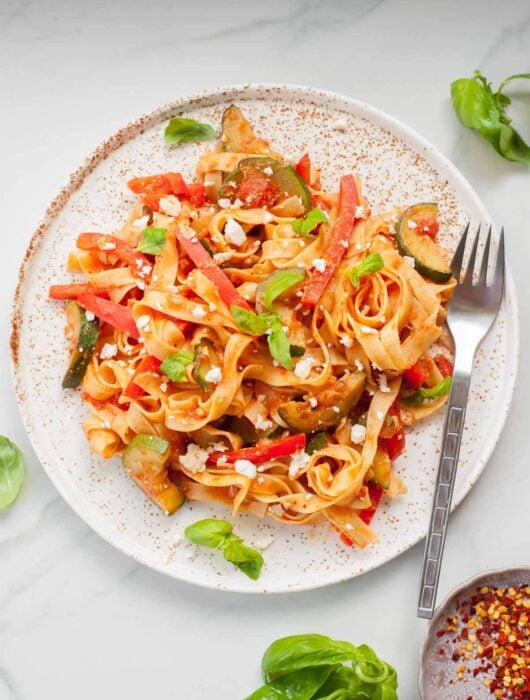Tagliatelle pasta with zucchini, bell pepper and feta on a white plate.