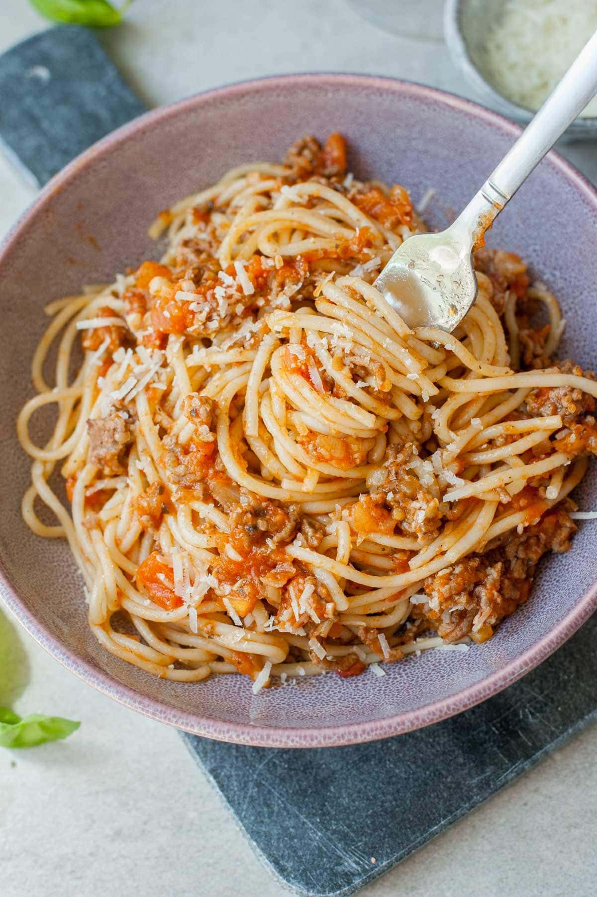 Spaghetti with fresh tomato meat sauce on a fork in a violet bowl.