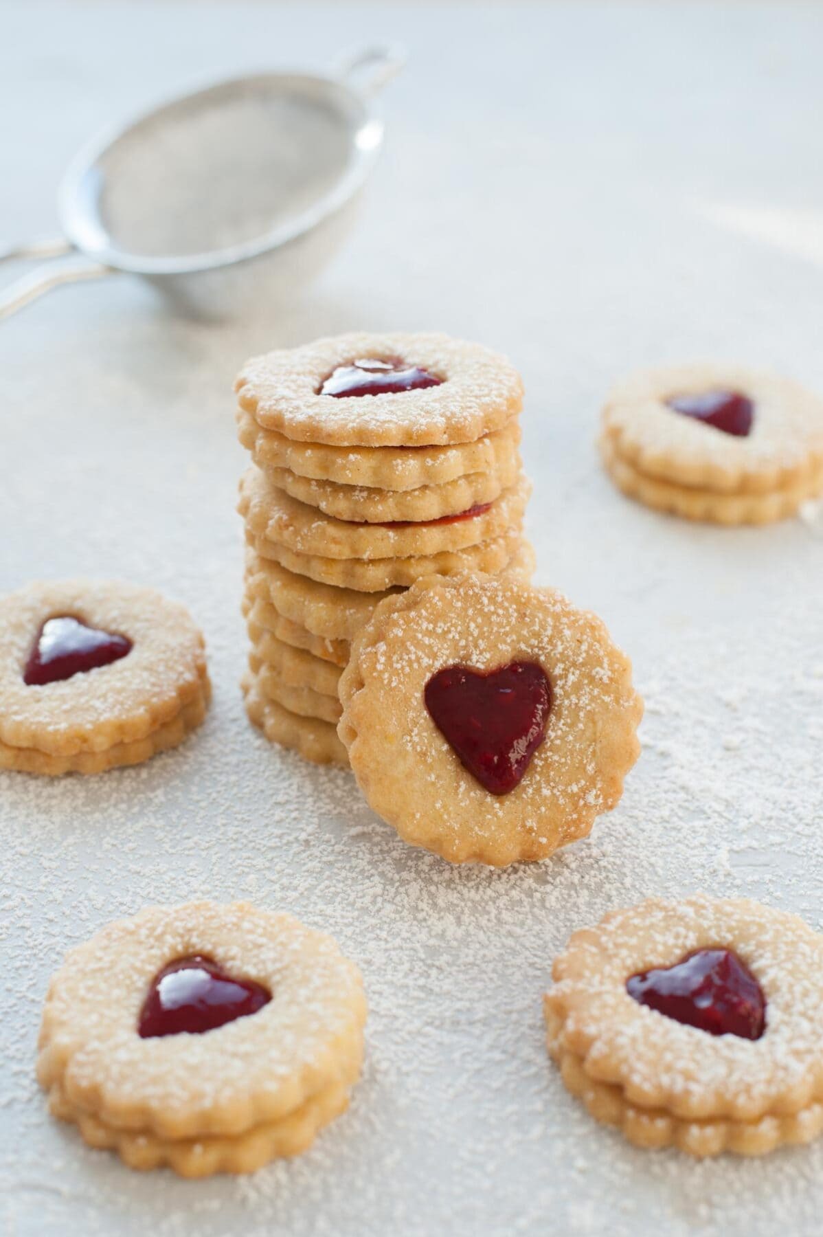 A stack of Linzer cookies. Heart-shaped Linzer cookies scattered around.