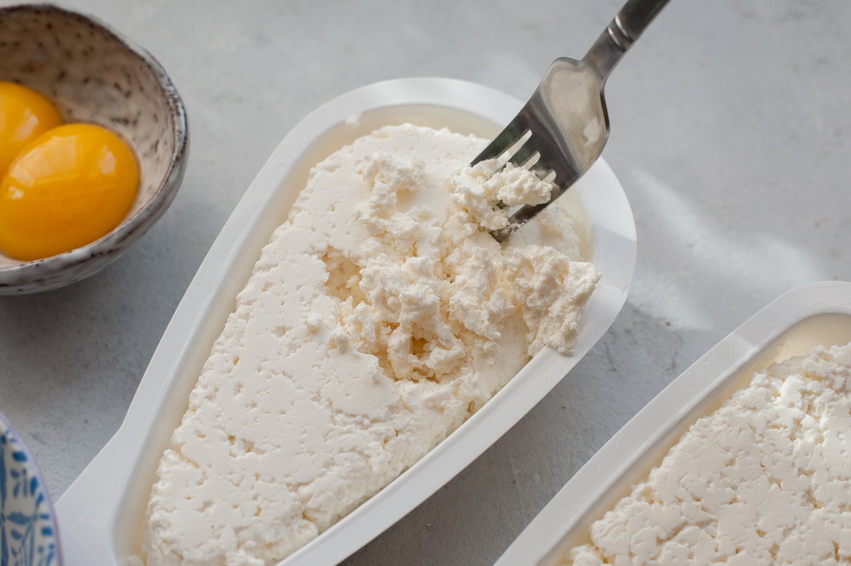 Polish twarog cheese is being crumbled with a fork.