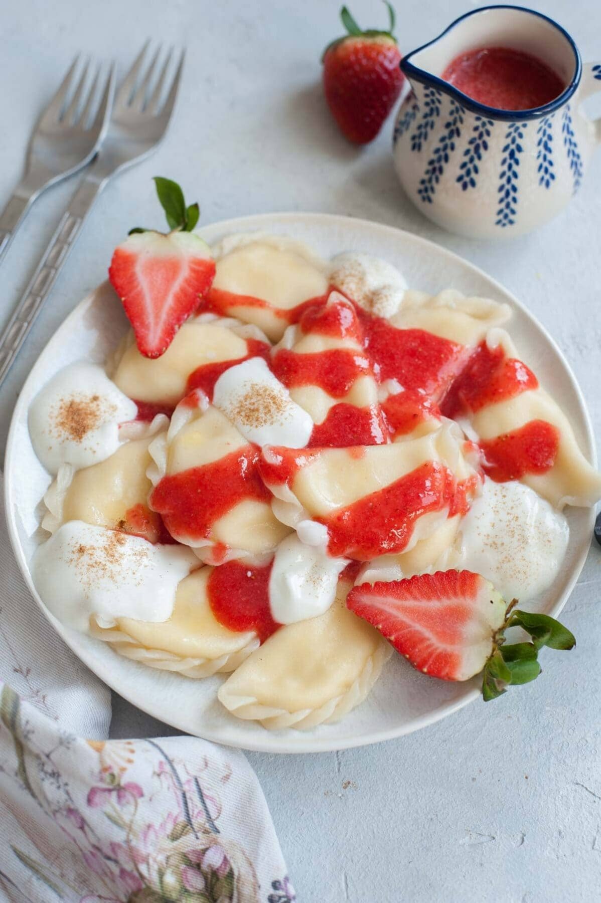 Sweet cheese pierogi on a white plate topped with strawberry sauce and whipped cream.