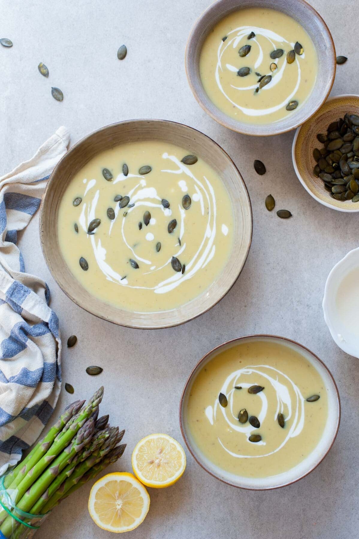 Three bowls with cream of asparagus soup topped with goat cheese and pepitas.