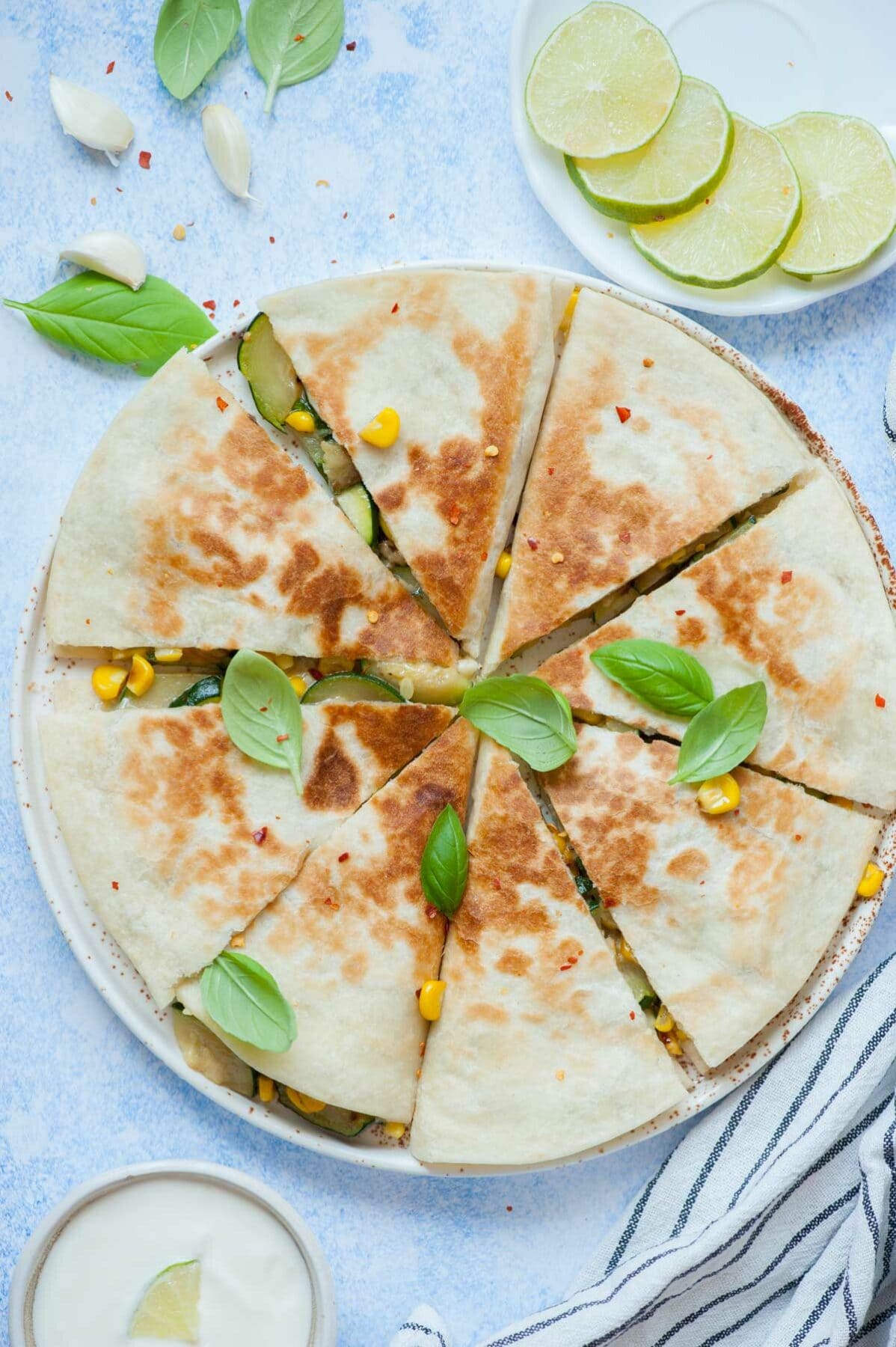 Zucchini quesadillas cut into triangles on a white plate, topped with basil leaves.