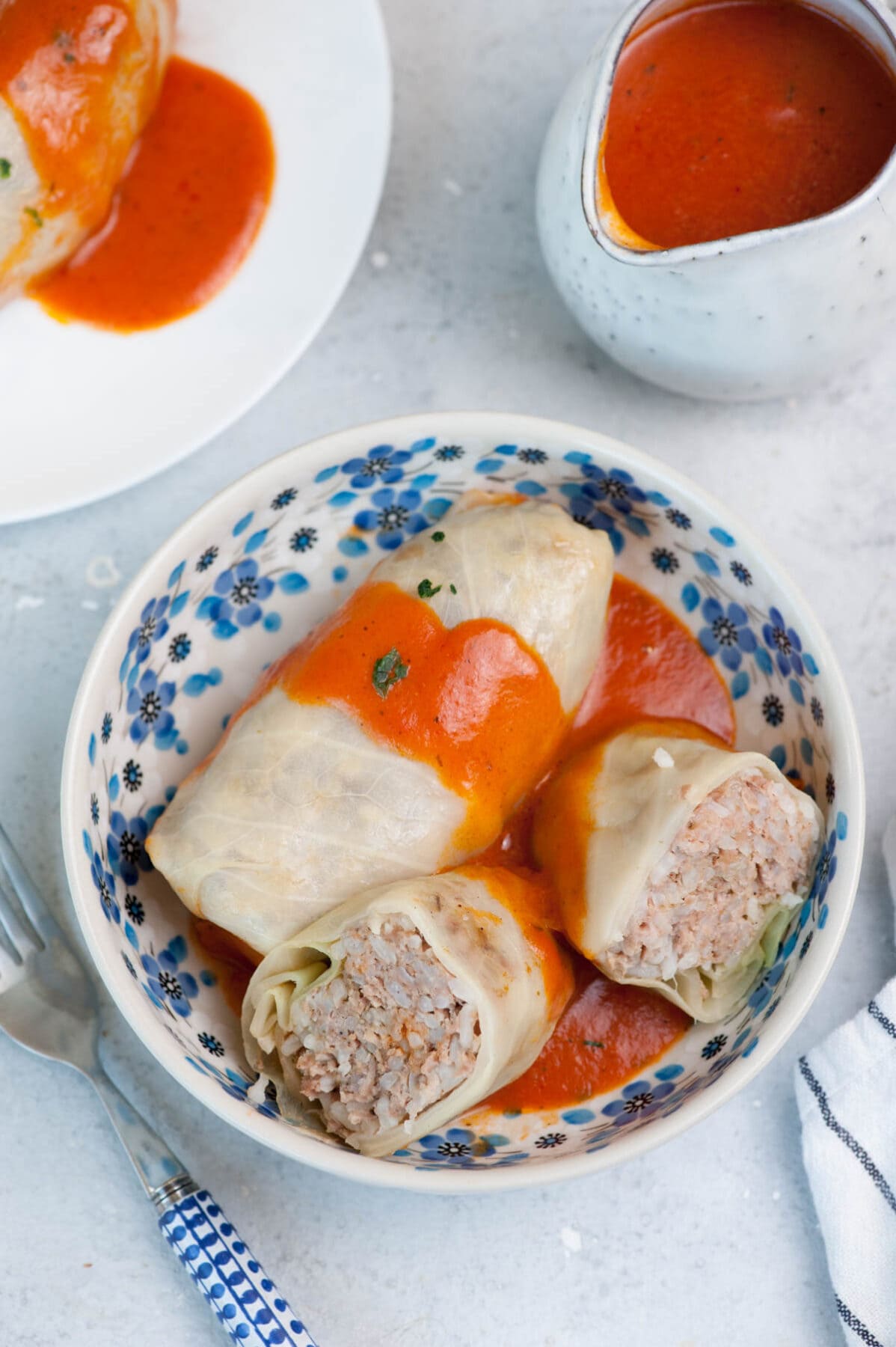Gołąbki Polish Stuffed Cabbage Rolls in a white bowl. A saucier with tomato sauce in the background.