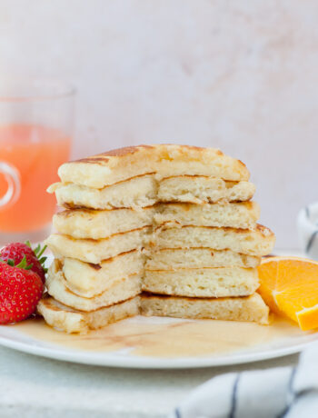 A stack of buttermilk pancakes with a part missing on a white plate.