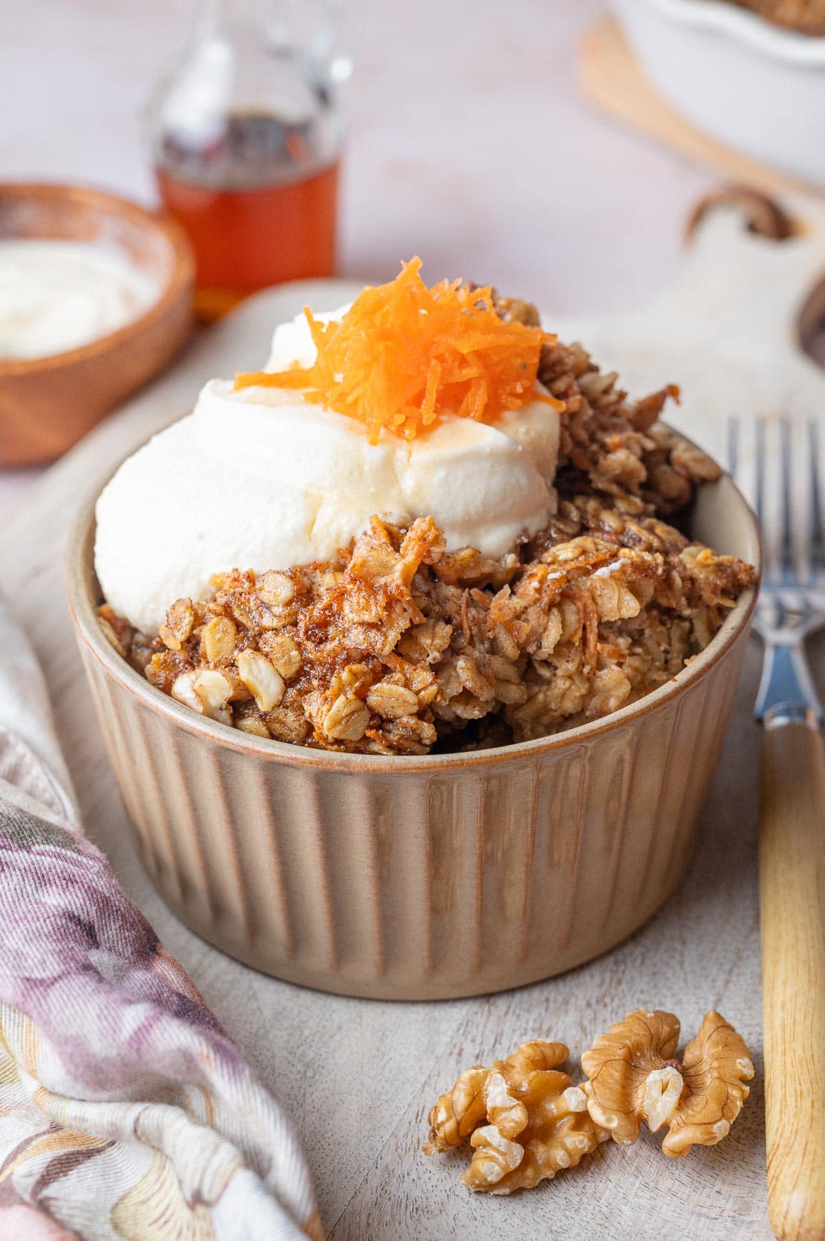 Carrot cake baked oatmeal in a brown bowl topped with cream cheese topping and grated carrots.
