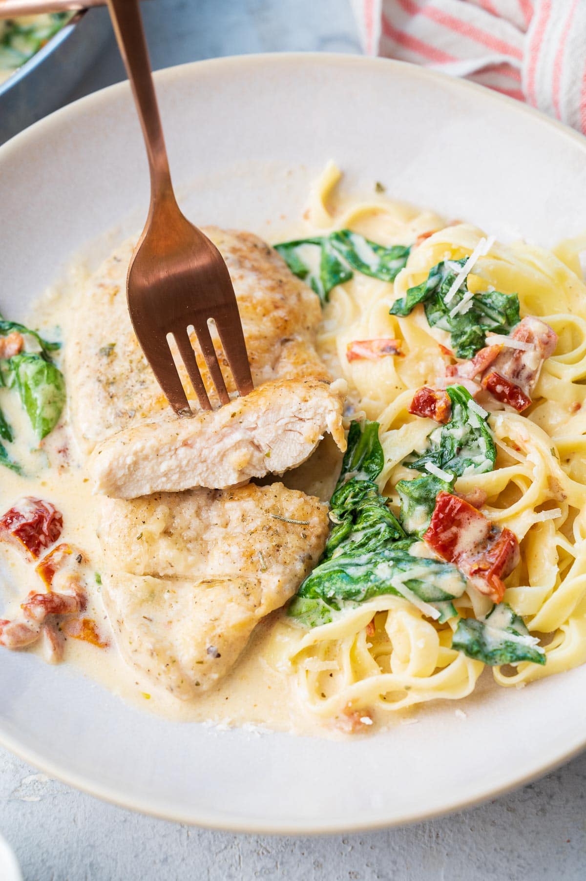 Tuscan chicken pasta on a beige plate. The chicken is stuck on a fork.
