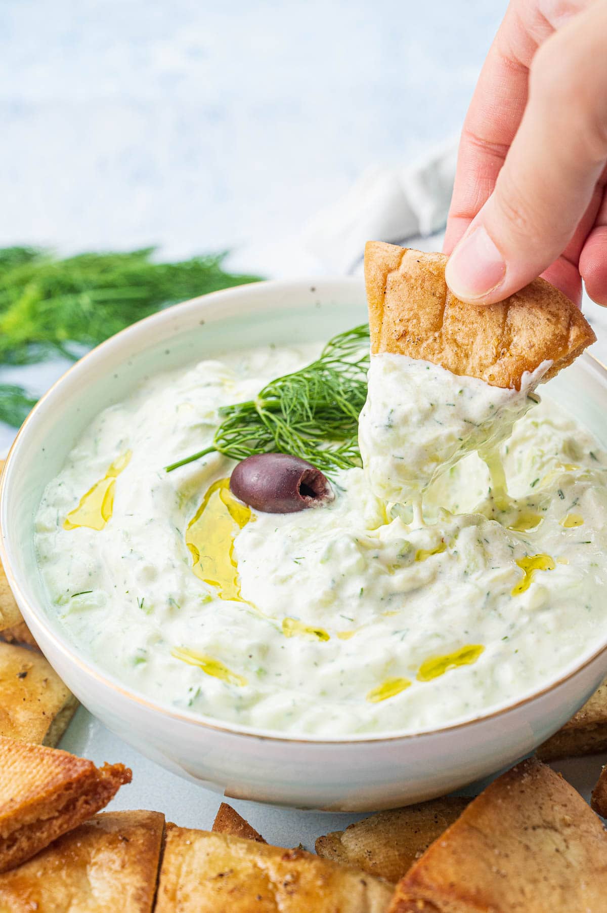 Tzatziki dip in a bowl is being scooped with a pita chip.