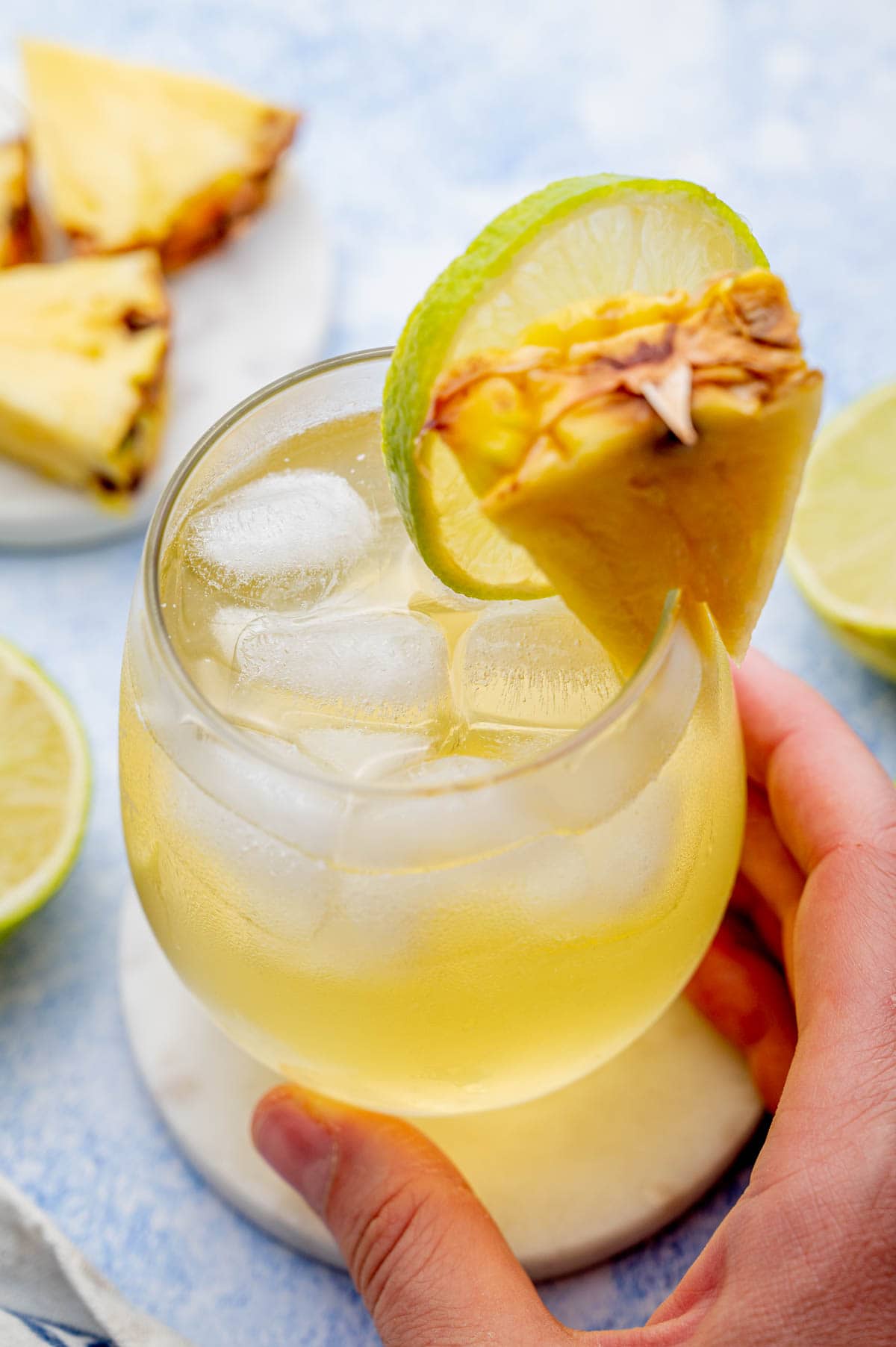 Pineapple vodka drink in a glass garnished with a pineapple wedge and a lime slice.