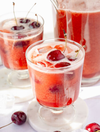 Two glasses and a pitcher with cherry lemonade.