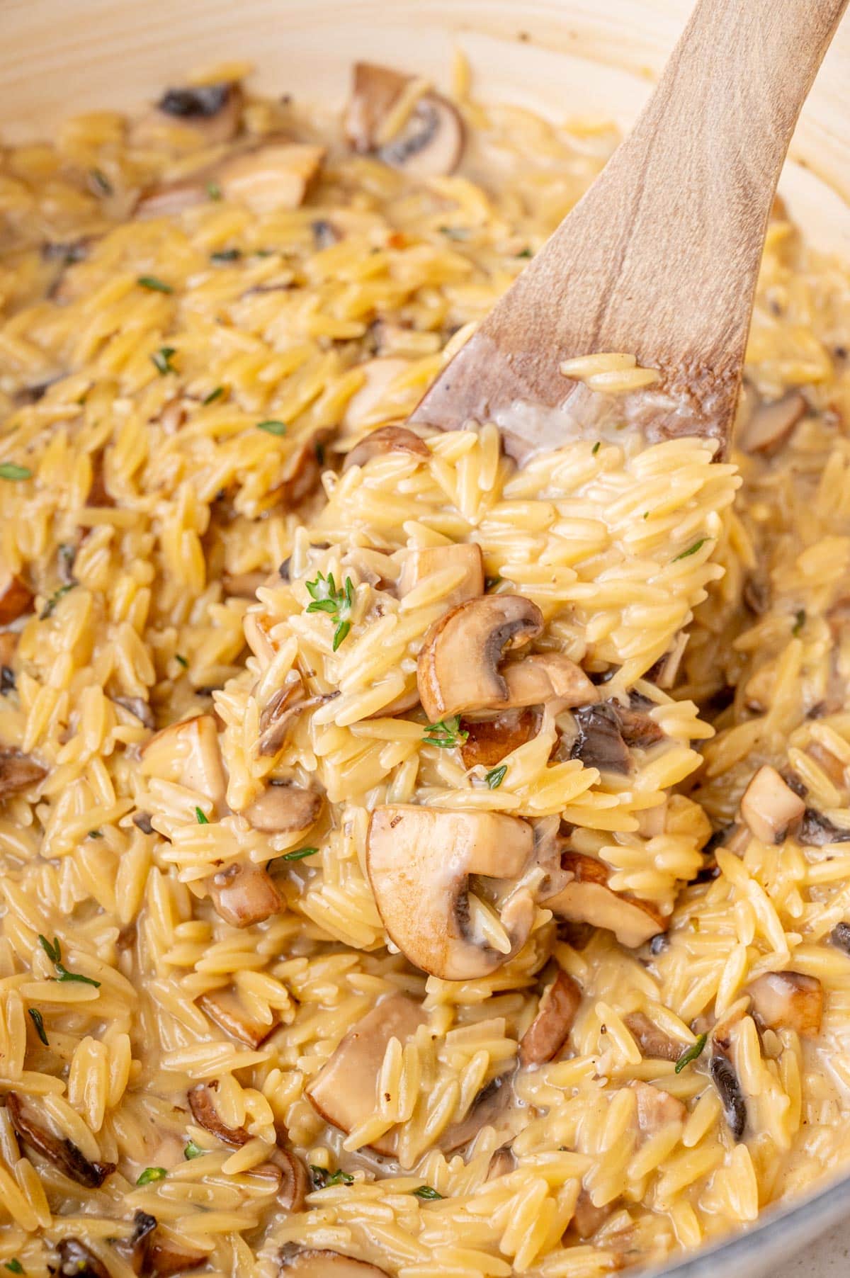 Mushroom orzo in a white pot with a wooden spatula.