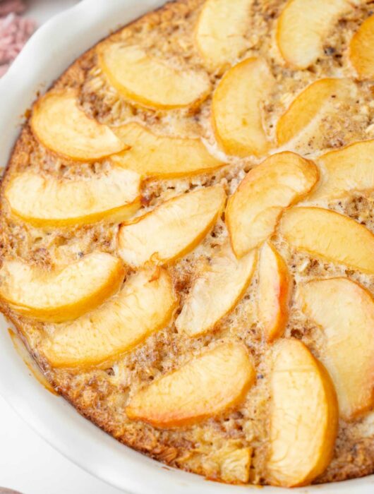 A close up photo of baked peach oatmeal in a white baking dish.