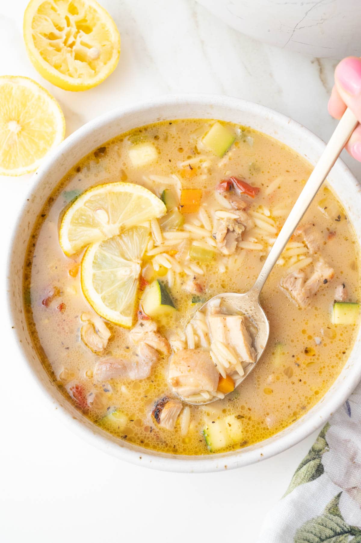 Lemon chicken orzo soup with lemon slices on top in a beige bowl.