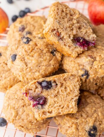 Freshly baked healthy breakfast muffins stacked on a wire cooling rack, with one muffin cut in half to show its soft and moist texture with visible blueberries inside.