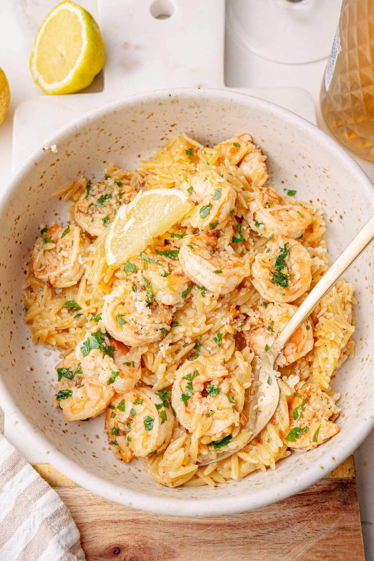 Bowl of shrimp scampi orzo garnished with lemon wedge and fresh parsley, served with a fork.
