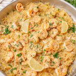 Shrimp scampi orzo served in a large skillet, topped with lemon wedges and chopped parsley, ready to serve.