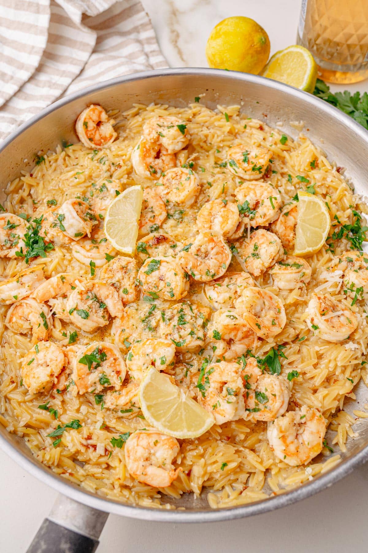 Shrimp scampi orzo served in a large skillet, topped with lemon wedges and chopped parsley, ready to serve.

