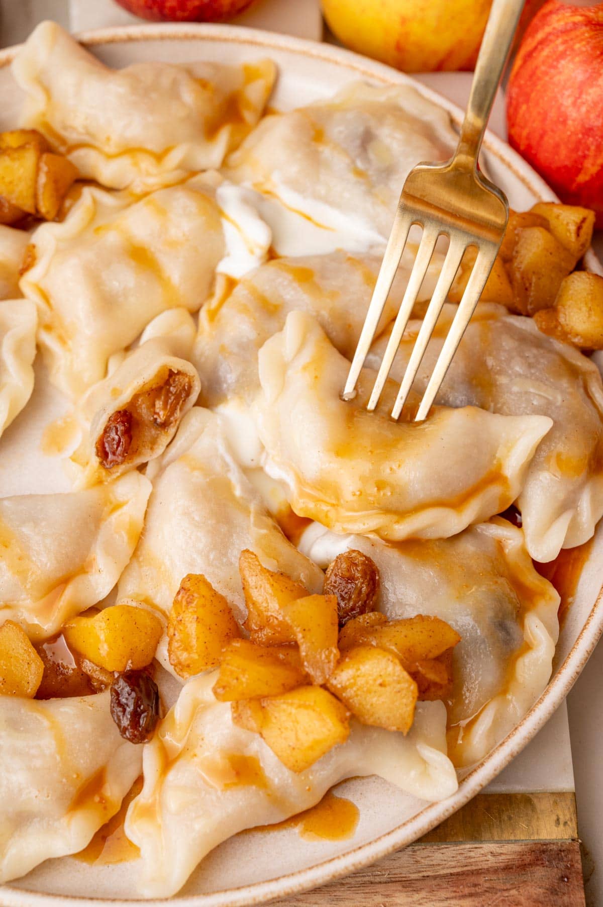 Apple pierogi on a beige plate served with sour cream and caramel sauce. One pierogi stuck on a fork.