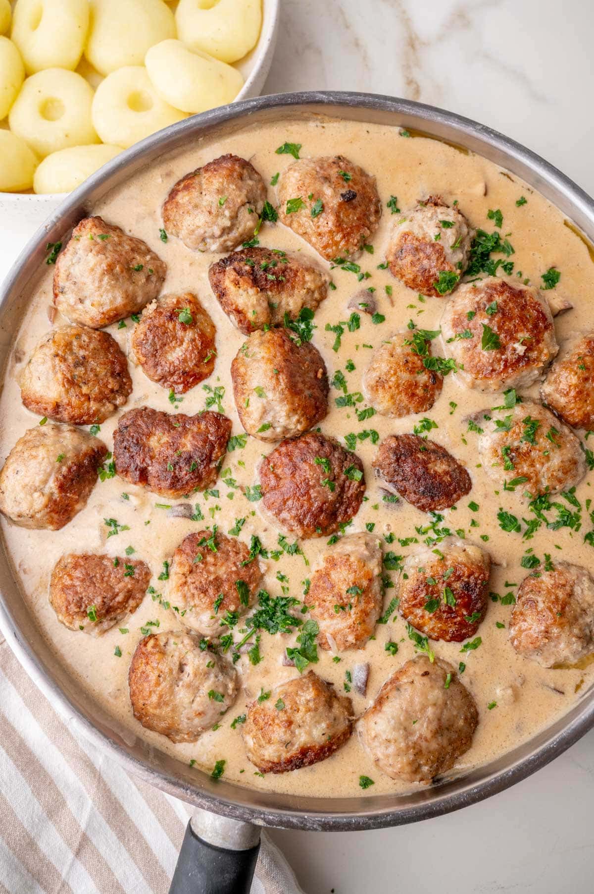 Meatballs with mushroom sauce in a large frying pan. Silesian Dumplings in the background.