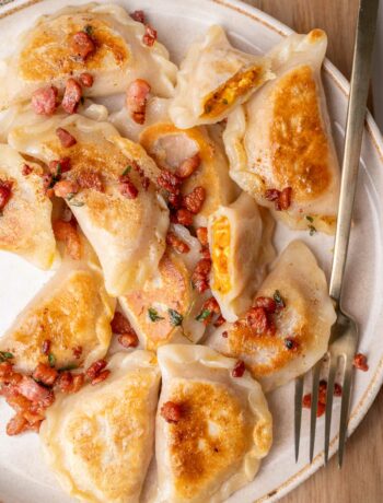 Pumpkin pierogi topped with crispy guanciale on a beige plate.