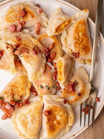 Pumpkin pierogi topped with crispy guanciale on a beige plate.