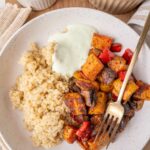 Sweet potatos with bell pepper and mushrooms, served with quinoa and yogurt sauce on a white plate.