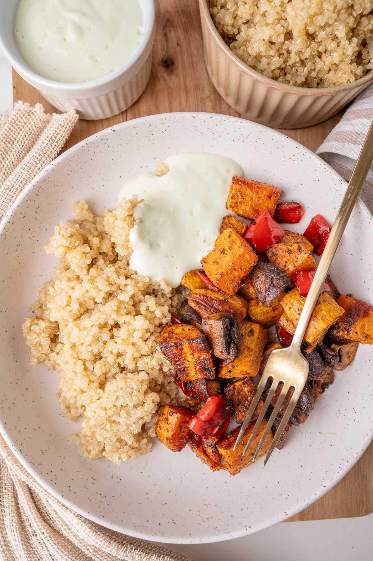 Sweet potatos with bell pepper and mushrooms, served with quinoa and yogurt sauce on a white plate.